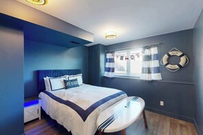 Une chambre à coucher avec un lit, une table de chevet, une fenêtre avec des rideaux et un objet décoratif en forme de bouée de sauvetage.