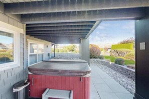 Ein überdachter Außenbereich mit Whirlpool, Fenster und Blick auf einen angelegten Garten.