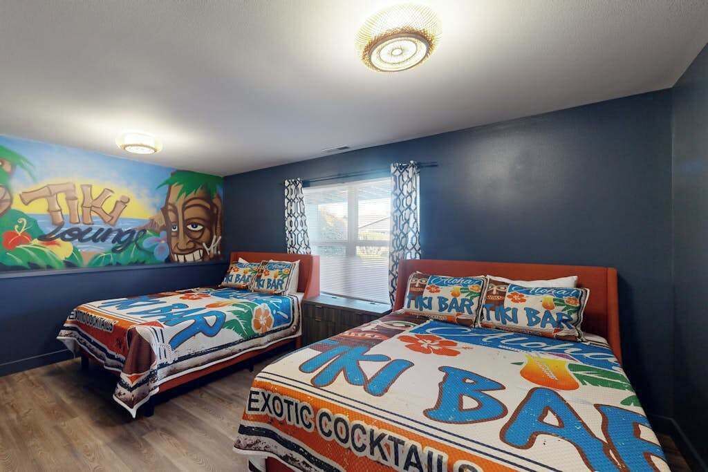 Ein Zimmer mit zwei Betten, jedes mit einer farbenfrohen Tagesdecke mit tropischen Motiven und Cocktail-Designs.