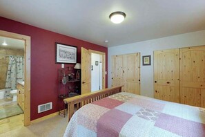 A bedroom with a bed, wooden wardrobe, and a bathroom visible through an open door. - 2BR A-Frame - Fireplace - Patio - W&D (Leavenworth)