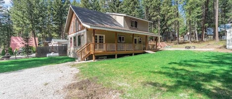 A two-story log cabin with a porch and a fenced yard.