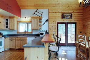 A wooden cabin interior with a kitchen, dining area, and a large window. - 2BR A-Frame - Fireplace - Patio - W&D (Leavenworth)