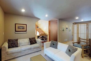 Ein Wohnzimmer mit zwei Sofas, einem Holzstuhl und einer Treppe zu einer oberen Ebene.