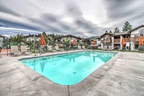 Uma piscina com espreguiçadeiras e guarda-sóis, rodeada por edifícios com varandas.