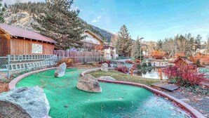 A rustic cabin with a wooden exterior, surrounded by a natural landscape with trees and a small pond. - 1 BR condo located in Icicle Village, Leavenworth (Leavenworth)