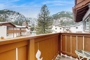Een balkon met uitzicht op besneeuwde bergen en een dennenboom.