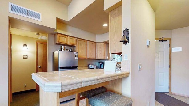 A kitchen with wooden cabinets, a stainless steel refrigerator, and a countertop with a bench. - 1 BR condo located in Icicle Village, Leavenworth (Leavenworth)