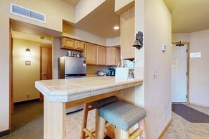 A kitchen with wooden cabinets, a stainless steel refrigerator, and a countertop with a bench. - 1 BR condo located in Icicle Village, Leavenworth (Leavenworth)