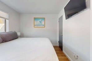 A bedroom with a bed, a wall-mounted TV, a door, and a framed picture on the wall. - Cozy 1BR Lakeview - Balcony - Pool - (Chelan)