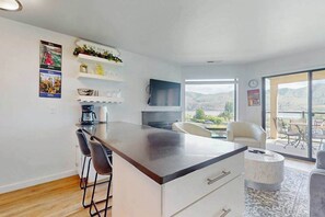 A modern kitchen with a bar area, a flat-screen TV, and a view of the outdoors. - Cozy 1BR Lakeview - Balcony - Pool - (Chelan)