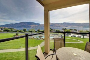 A balcony with a table and chairs, overlooking a pool and a view of mountains and a body of water. - Cozy 1BR Lakeview - Balcony - Pool - (Chelan)