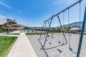 Ein Spielplatz mit Schaukeln und Pool, umgeben von Häusern und Hügeln.
