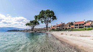Ein Küsteneigentum mit klarem Wasser, einem Sandstrand und einer Reihe Häuser mit roten Dächern.