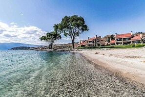 A coastal property with clear waters, a sandy beach, and a row of houses with red roofs. - Bright 1BR Lakefront - Patio - Pool (Chelan)