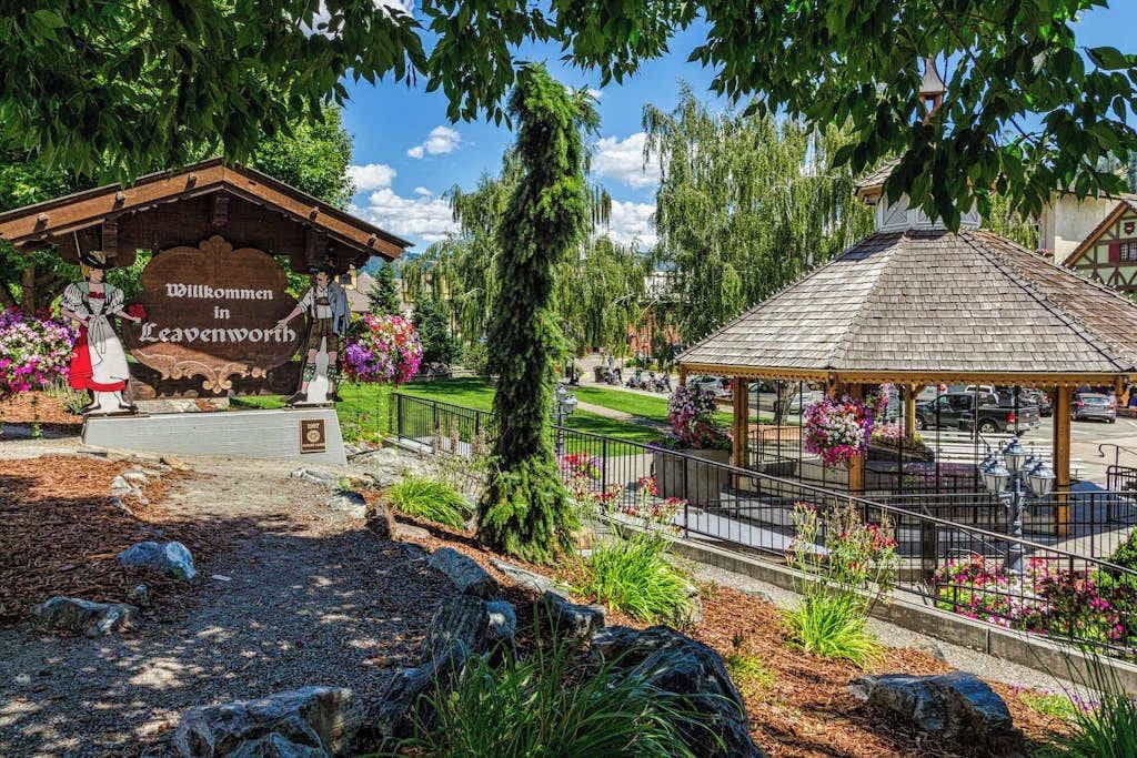 Ein traditionelles Holzgebäude mit einem Schild, das Besucher in Leavenworth willkommen heißt, umgeben von gepflegten Gärten und einem Gazebo.