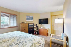 Een slaapkamer met een bed, een televisie, een bureau met computer en een raam met zonwering.