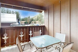 A balcony with a glass table and chairs, a view of a mountainous area, and a building in the background. - Sunny Studio Mountainview 2nd-Floor - Balcony (Leavenworth)
