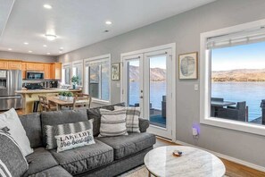 A modern living room with a gray sofa, a marble coffee table, and a view of a lake through large windows.