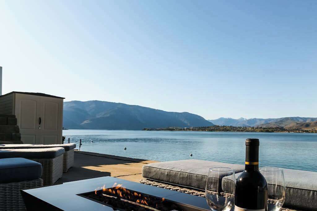 Eine See-Terrasse mit Feuerstelle, Sitzgelegenheiten und einer Weinflasche.