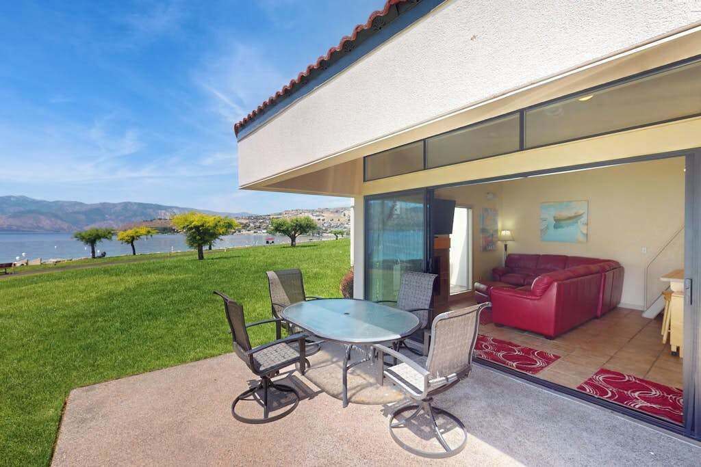 Eine Terrasse im Freien mit einer Glastür zu einem Wohnbereich, einem Tisch mit Stühlen und einem roten Sofa.