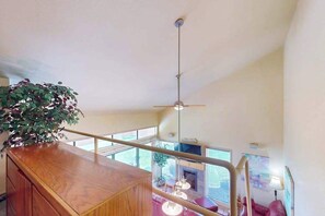 A high-ceilinged room with a wooden desk, a hanging plant, and a view through large windows. - Studio Lakefront 1st-floor - Patio - Pool (Chelan)