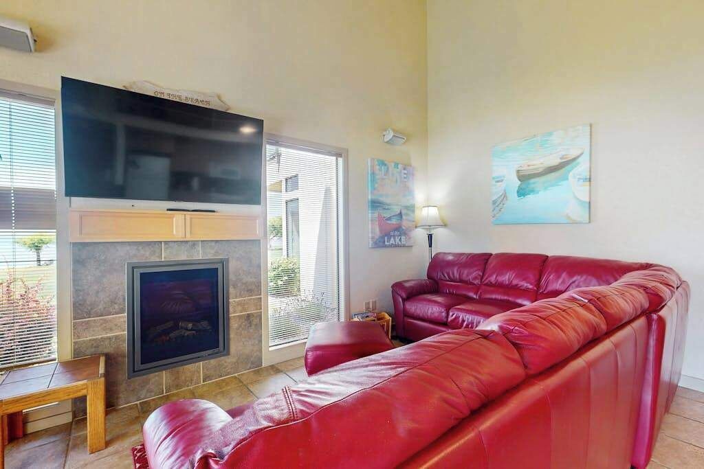 Una sala de estar con un sofá de cuero rojo, un televisor de pantalla plana sobre una chimenea y obras de arte en las paredes.