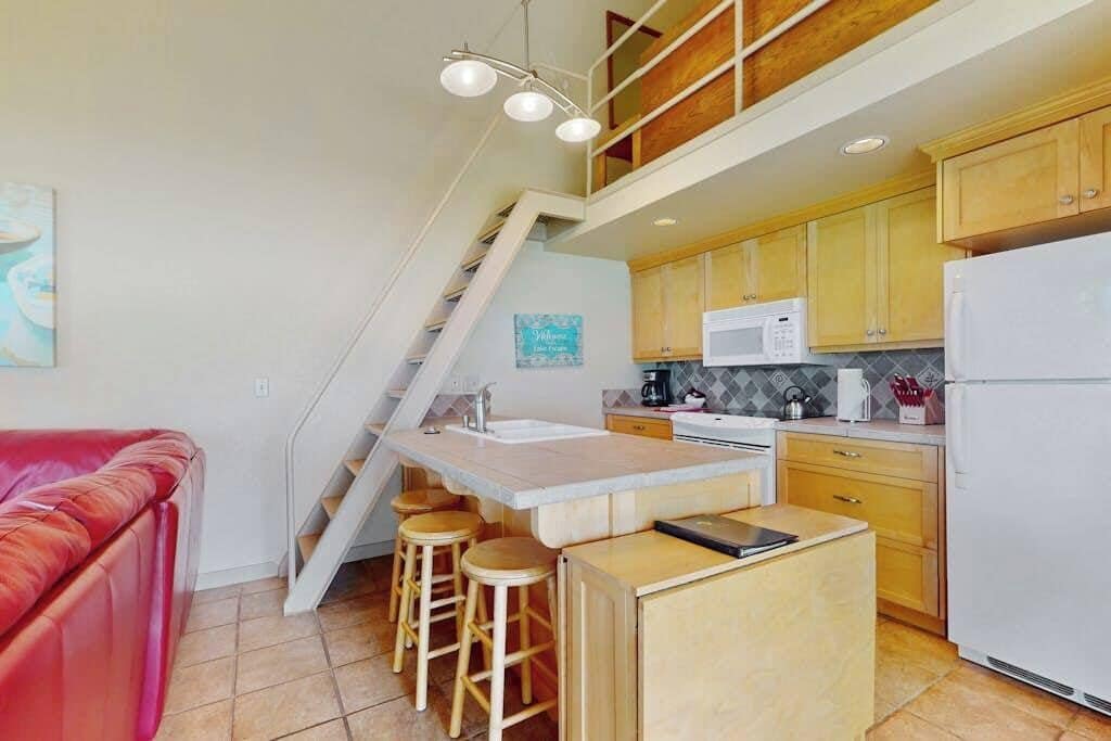 Una cocina con una isla central, armarios de madera, microondas y refrigerador.