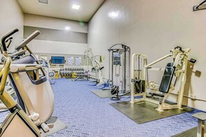 Un gimnasio con varias máquinas de ejercicio, un televisor y un monitor de computadora en la pared.