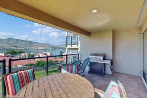Ein Balkon mit Blick auf ein Gewässer und Hügel, inklusive Grill und Tisch mit Stühlen.