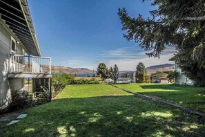 A residential property with a grassy yard, a balcony, and a view of a lake and hills.