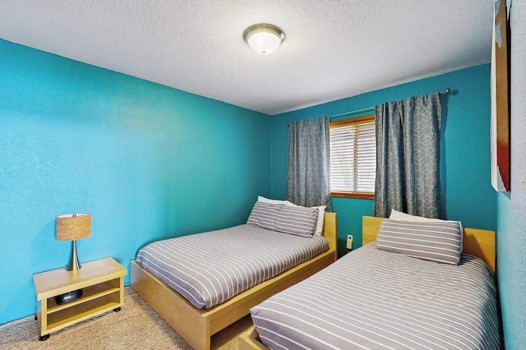 A room with two beds, a nightstand, a lamp, and a window with curtains.
