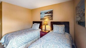 Quarto de hotel com duas camas, uma mesa de cabeceira com abajur e um quadro na parede.