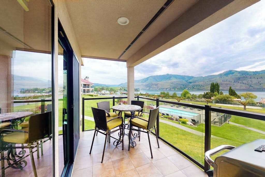 A balcony with a table and chairs, overlooking a landscape with hills and a body of water.