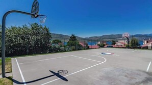 Quadra de basquete ao ar livre com vista para um lago e montanhas ao fundo.
