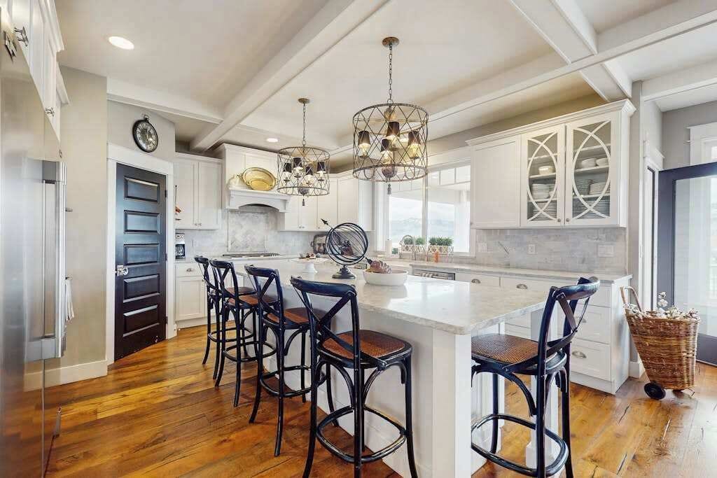 A kitchen with a large island, bar stools, pendant lighting, and white cabinetry.