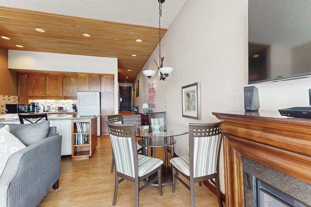 Una cocina moderna con armarios de madera, un comedor con mesa de vidrio y sillas a rayas, y una chimenea empotrada.