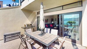 An outdoor patio with a table and chairs, a grill, and a view of the interior. - Stylish 1BR Lakefront - Patio - Pool (Chelan)