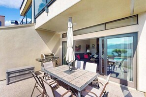 An outdoor patio with a table and chairs, a grill, and a view of the interior. - Stylish 1BR Lakefront - Patio - Pool (Chelan)