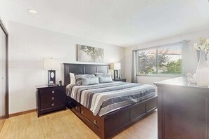 A bedroom with a bed, bedside tables, a window with blinds, and a view of greenery outside. - Stylish 1BR Lakefront - Patio - Pool (Chelan)
