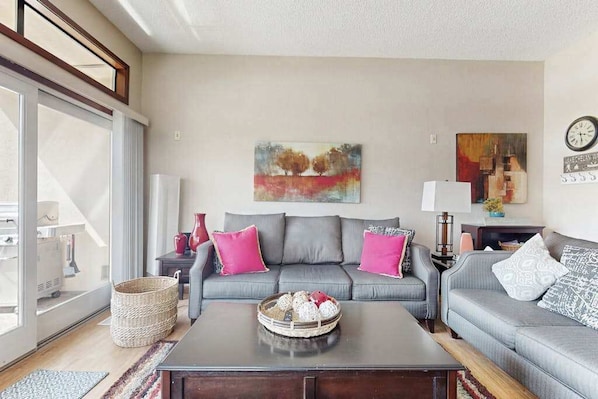 A living room with a grey sofa, a coffee table, and a painting on the wall. - Stylish 1BR Lakefront - Patio - Pool (Chelan)