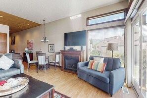 A modern living room with a fireplace, a flat-screen TV, and a large window. - Stylish 1BR Lakefront - Patio - Pool (Chelan)
