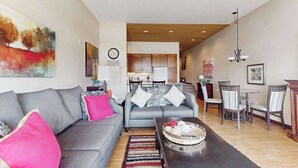 A modern living room with a grey sofa, a coffee table, and a dining area with chairs and a table. - Stylish 1BR Lakefront - Patio - Pool (Chelan)