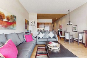 A modern living room with a grey sofa, a coffee table, and a dining area with chairs and a table. - Stylish 1BR Lakefront - Patio - Pool (Chelan)