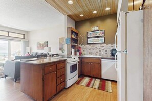 A modern kitchen with wooden cabinets, a central island, and a white refrigerator. - Stylish 1BR Lakefront - Patio - Pool (Chelan)