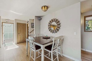 A dining area with a wooden table and white chairs, a decorative wall mirror, and a staircase in the background. - Huge 3BR Lakefront - Hot Tub - Dock - Deck (Chelan)