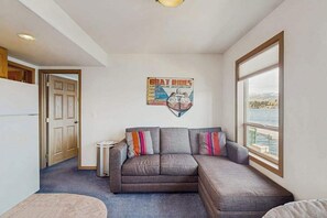 A living room with a gray sofa, a small round table, and a window with a view of the water. - Huge 3BR Lakefront - Hot Tub - Dock - Deck (Chelan)