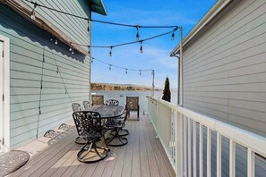 Une terrasse en bois avec une table et des chaises, une rambarde et des guirlandes lumineuses.