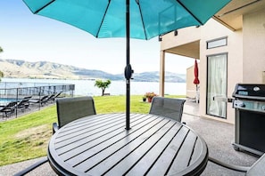 Et rundt bord med grill, parasol og udsigt til en sø med bjerge i baggrunden.
