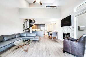 A modern living room with a spiral staircase, a sofa, a glass coffee table, and a fireplace. - 2BR Lakefront - Patio - Pool - Hot Tub - Dock (Chelan)