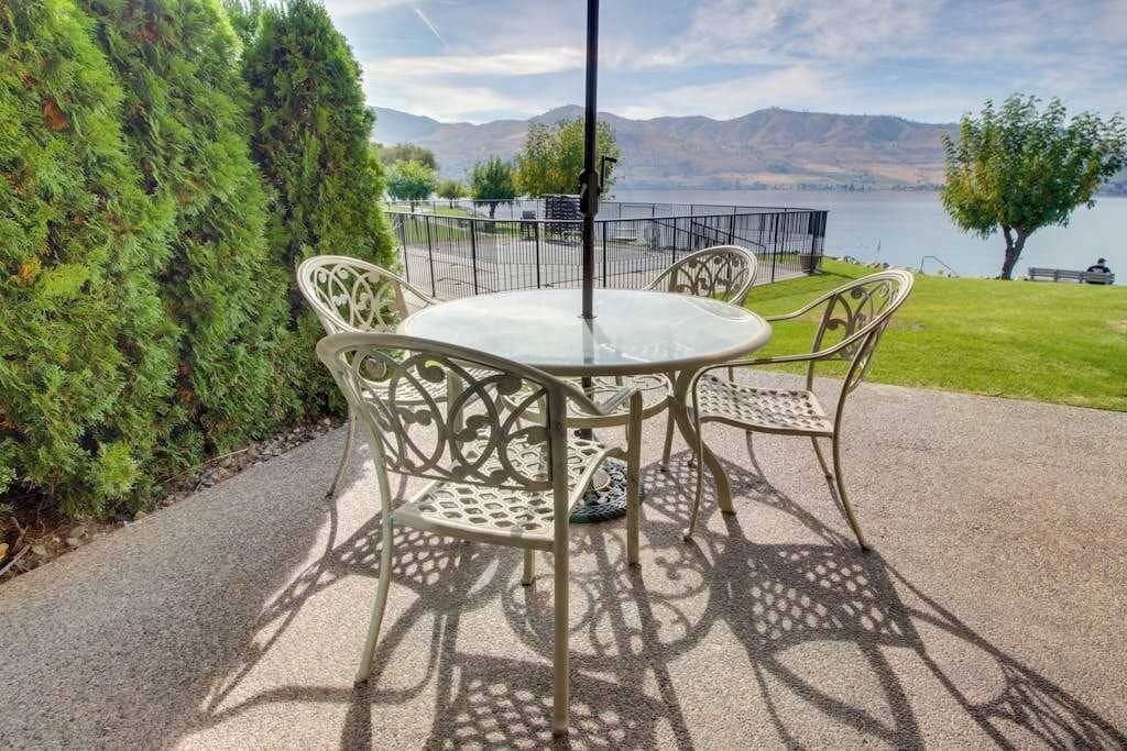 Eine Terrasse mit rundem Tisch und Stühlen, einem Metallzaun und Blick auf einen See mit Bergen im Hintergrund.